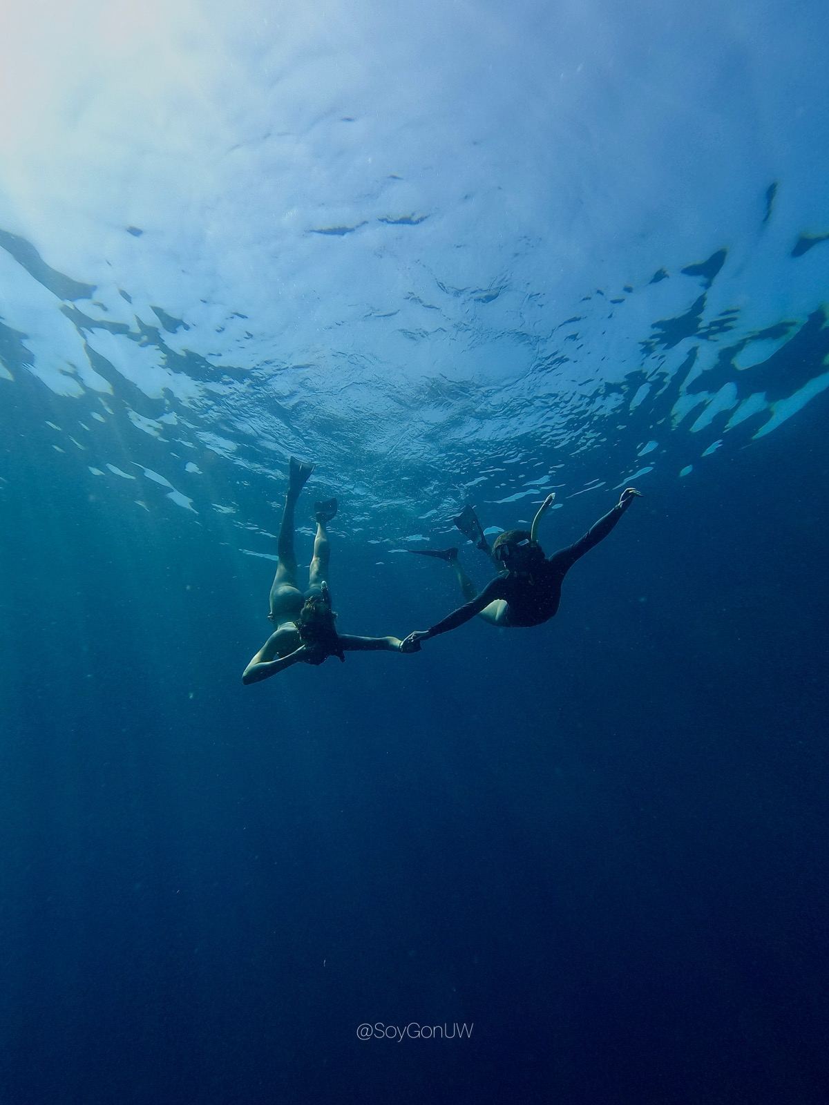 Two freedivers descending into deep blue water